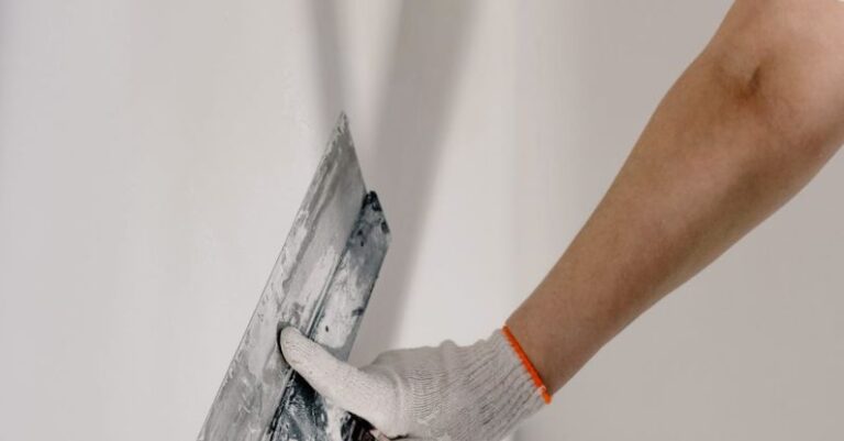 Improvements - Crop anonymous male worker in gloves holding putty knife while working at home