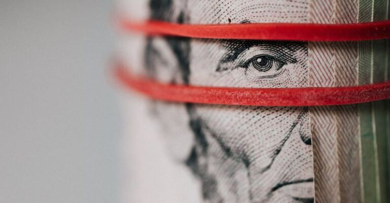 Income Approach - Closeup of rolled United States five dollar bills tightened with red rubber band