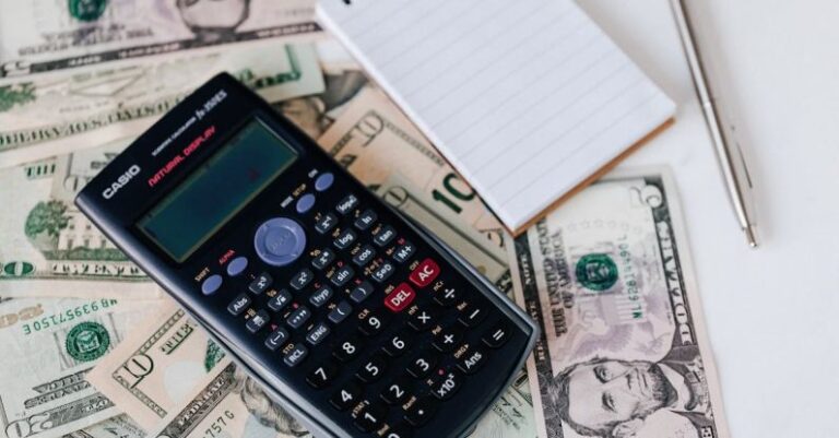 Loans - From above electronic calculator and notepad placed over United States dollar bills together with metallic pen for budget planning and calculation