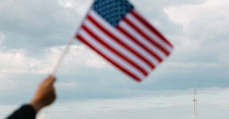 Equity - Crop unrecognizable patriot raising flag of USA on bright field